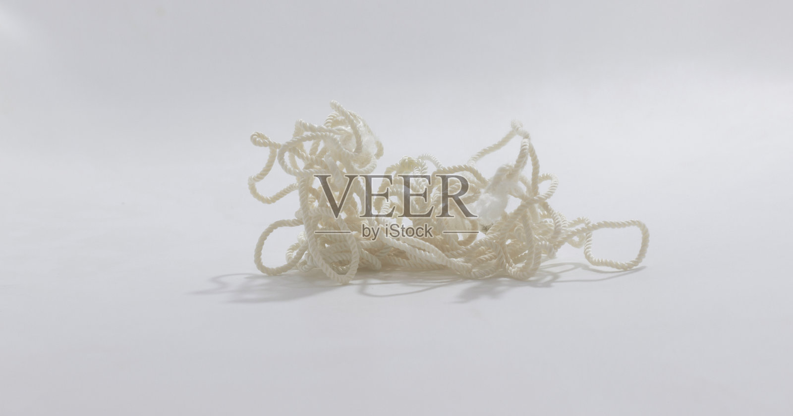 缠绕的白色绳索在简单背景上，投射出柔和的阴影，象征着混乱、困惑或复杂的局面。照片摄影图片