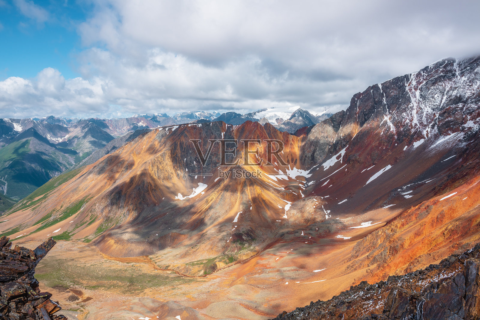 从岩石俯瞰到多彩的圆形山谷，弯曲的铁河流过，红色的尖锐岩脊耸立。五彩斑斓的大山脉覆盖着新落的雪。生动的高山在低云中若隐若现。照片摄影图片