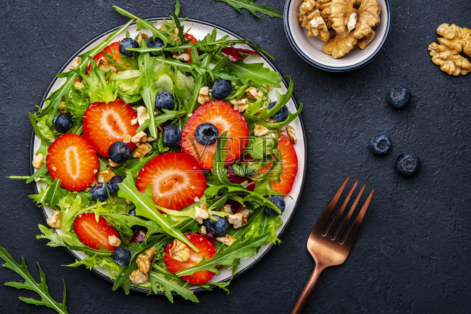 黑色背景上的素食草莓香草沙拉，配有芝麻菜、蓝莓和核桃。俯视图。照片摄影图片