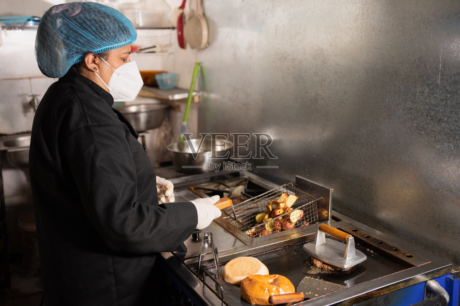 戴着口罩、帽子和手套的拉丁裔女性正在准备快餐照片摄影图片