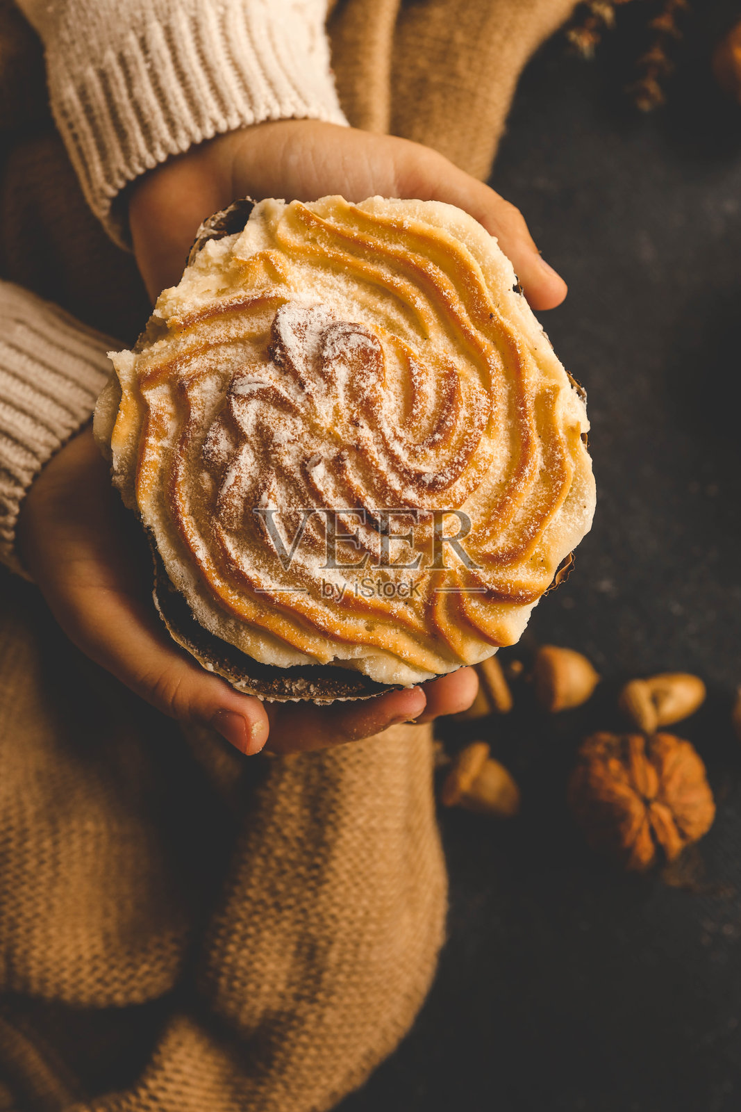 女孩在温馨的秋季环境中，手握一块撒了肉桂粉的甜面包，周围有橡果、蜡烛和干花，背景质感丰富，散发出温暖和舒适的氛围。照片摄影图片