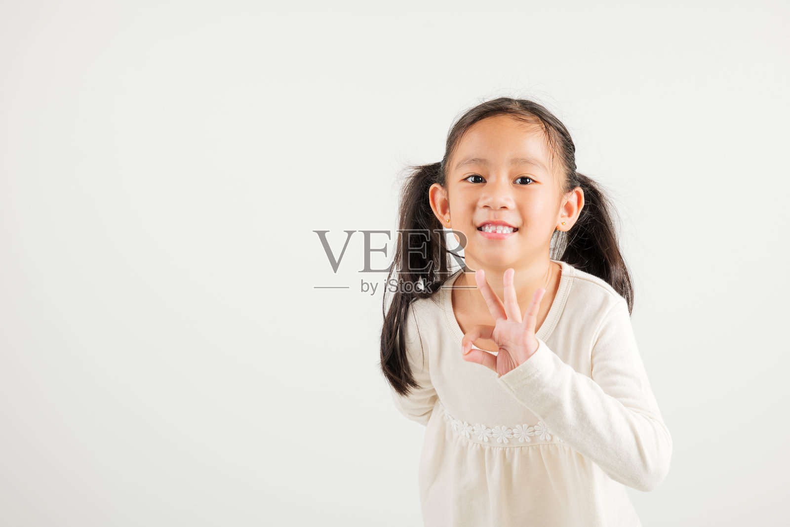 活泼的小女孩展示出OK手势，面带乐观的微笑，传达出同意和积极的情绪，背景为白色，非常适合您的文本定制。照片摄影图片