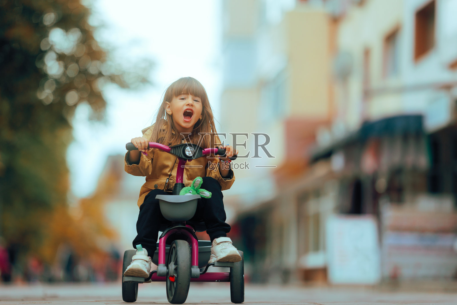 有趣的小女孩骑着三轮车，身边有她最喜欢的玩具照片摄影图片
