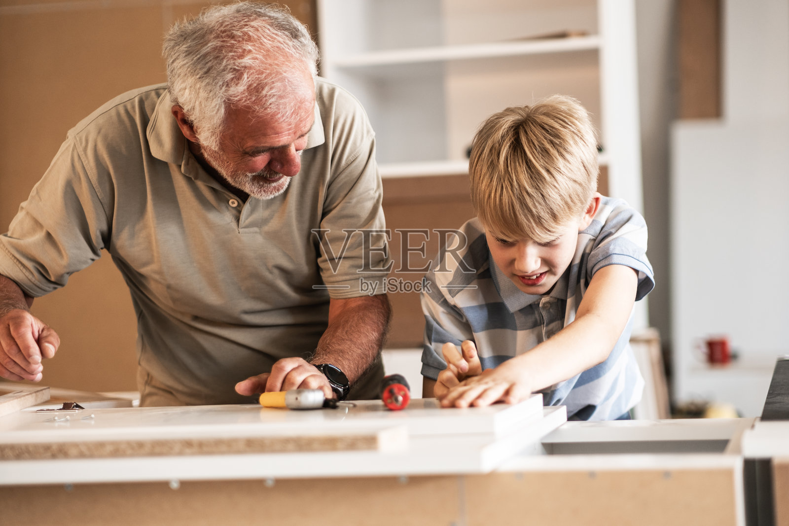 一位祖父在他的木工车间教孙子如何修理家具。照片摄影图片