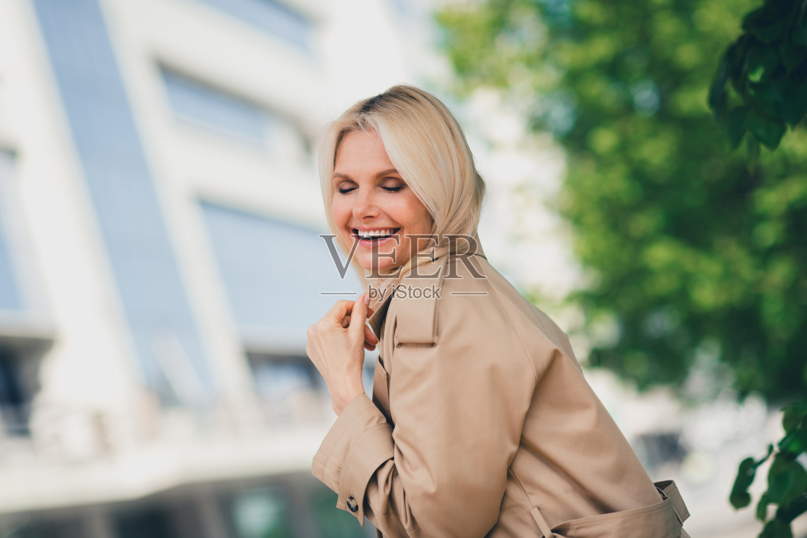 迷人的可爱退休女士在春天散步，轻触头发，享受护发，心情愉快，穿着米色外套，享受周末的户外闲暇时光。照片摄影图片