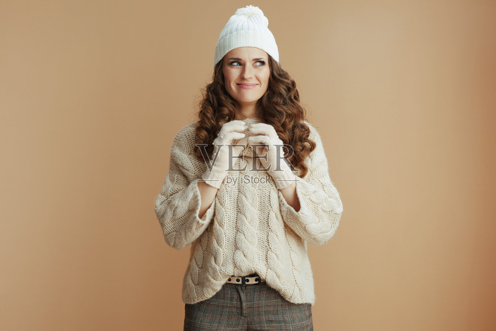 兴奋的女性穿着米色毛衣、手套和帽子，背景为米色。照片摄影图片