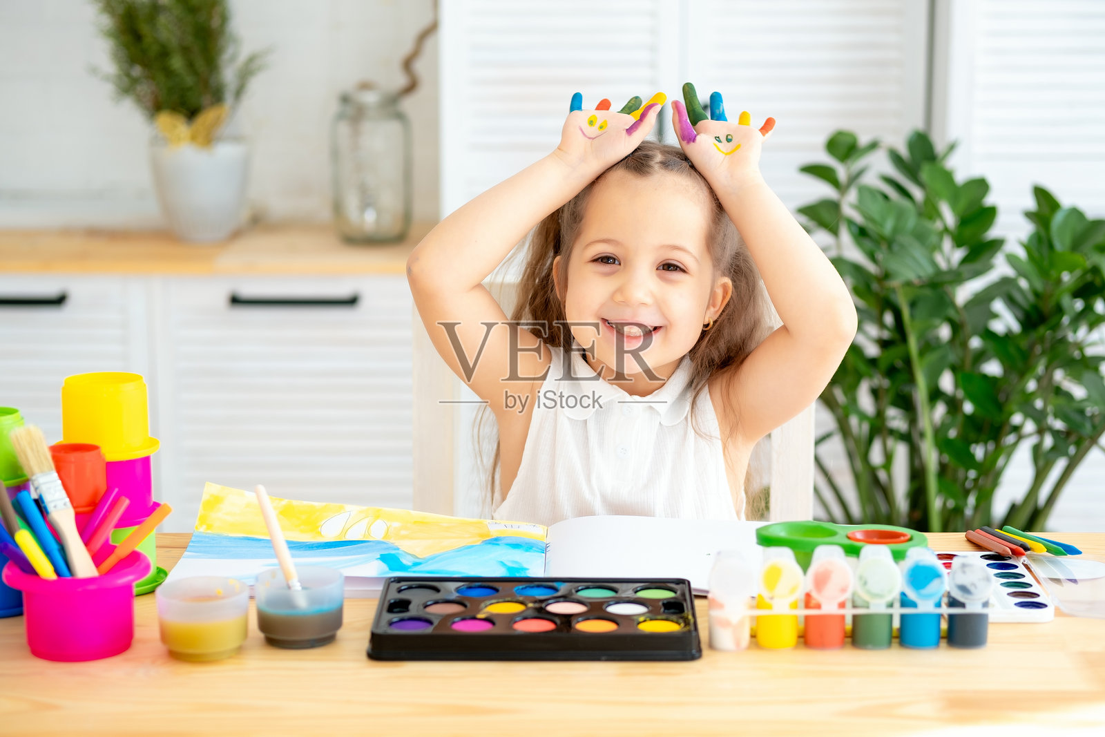 一个小女孩，手上沾满了颜料，正在通过玩耍学习绘画，她在艺术学校的绘画课上玩得很开心。照片摄影图片