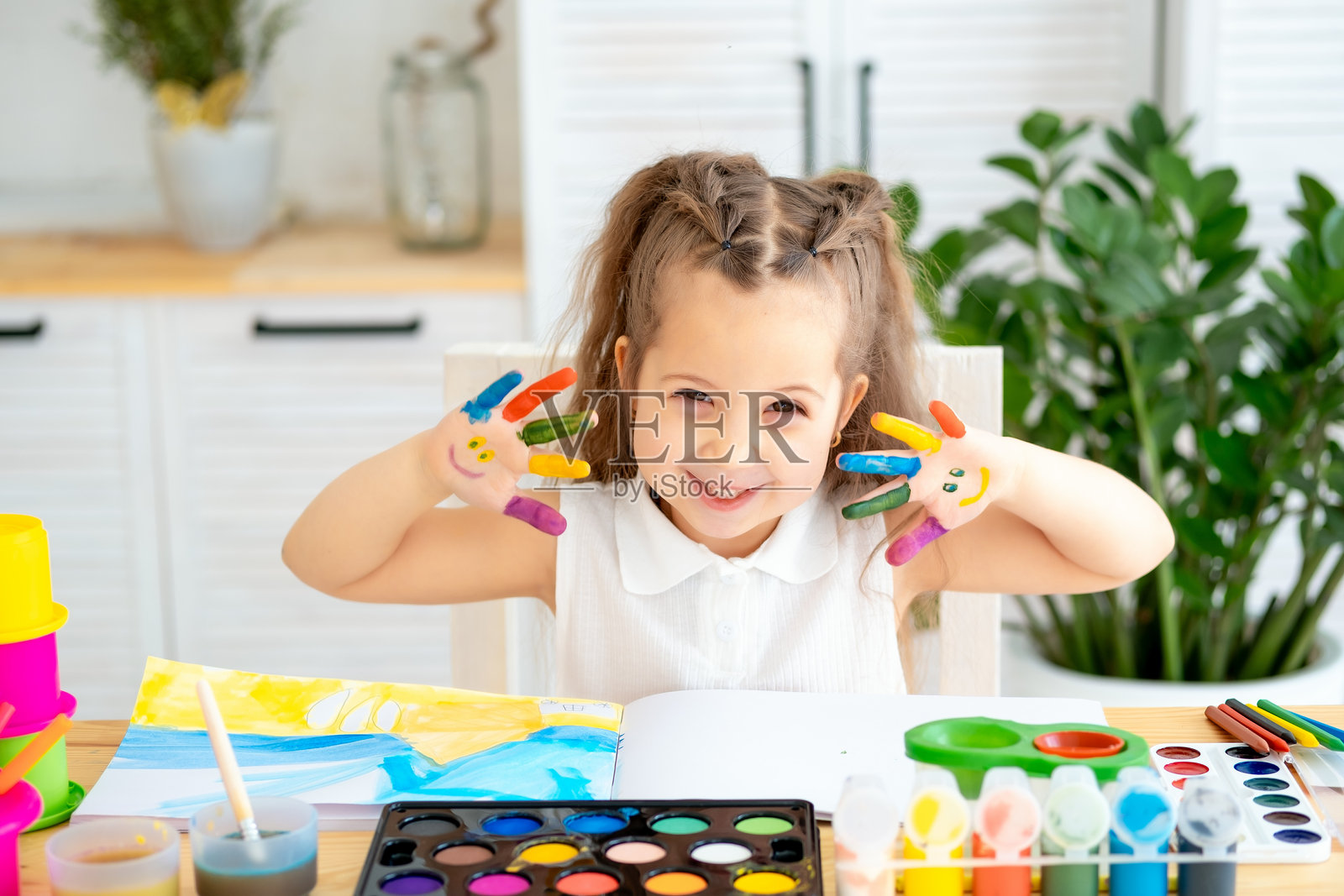 一个小女孩，手上沾满了颜料，正在通过玩耍学习绘画，她在艺术学校的绘画课上玩得很开心。照片摄影图片