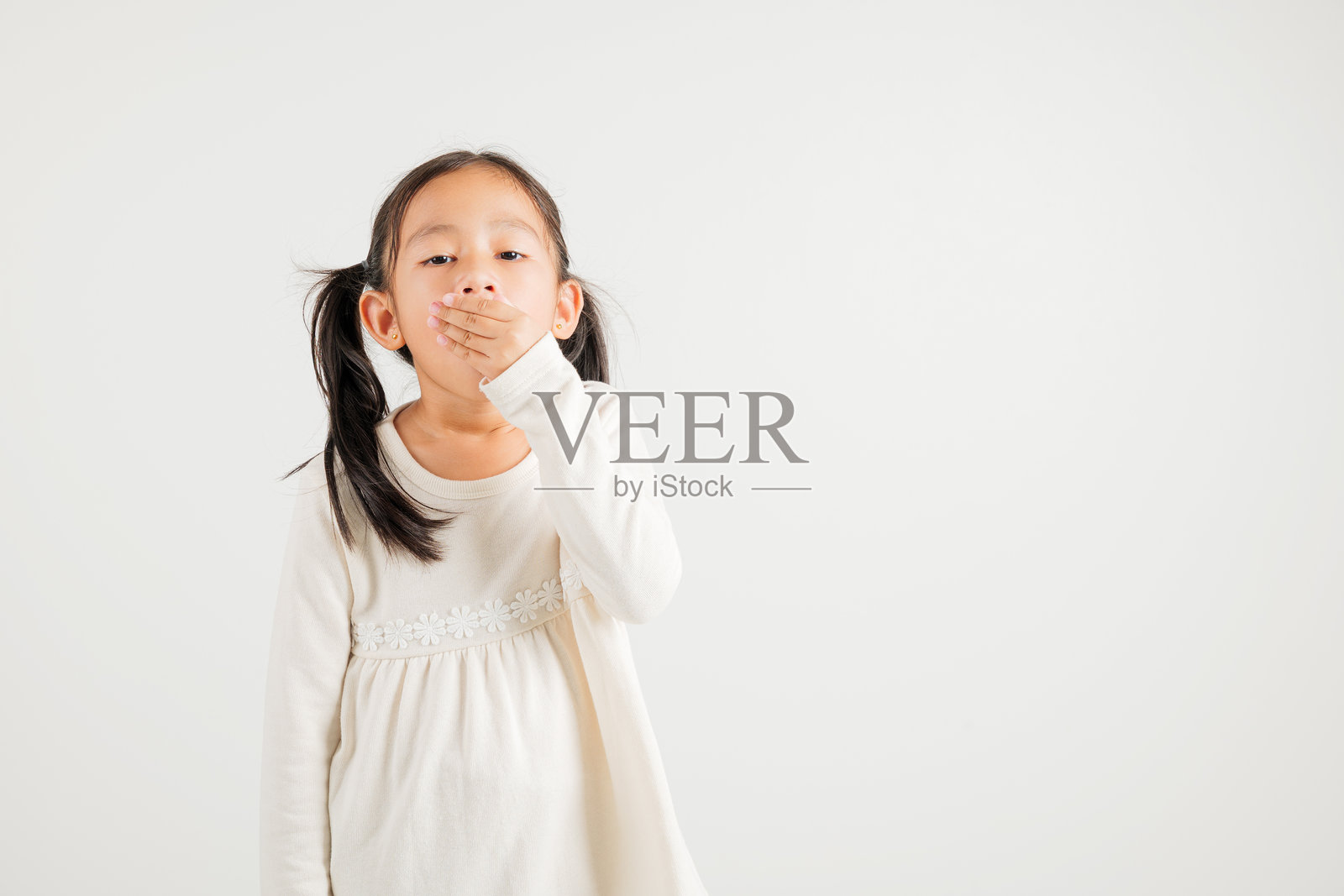 疲惫和困倦的亚洲小女孩肖像，打哈欠时用手捂住嘴，白色背景下的摄影，泰国幼儿园儿童失眠概念照片摄影图片