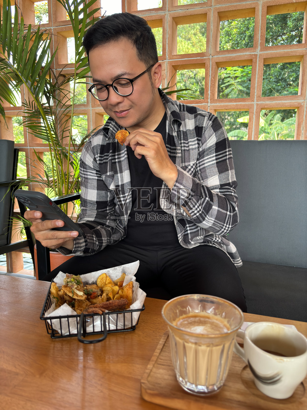 男人坐在咖啡馆里，一边吃零食一边看智能手机照片摄影图片