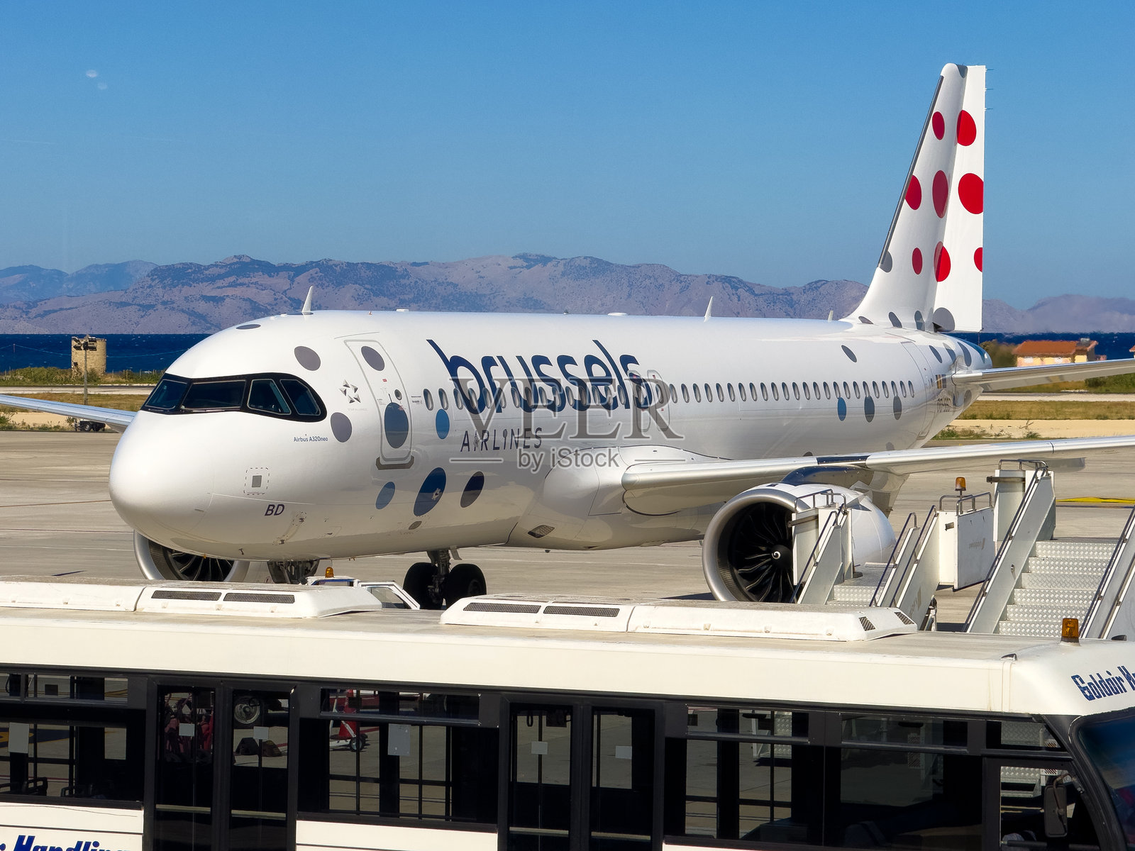 一架布鲁塞尔航空的空客A320停在机场的停机坪上,周围是宁静的风景,远处有山脉,头顶是湛蓝的天空。照片摄影图片