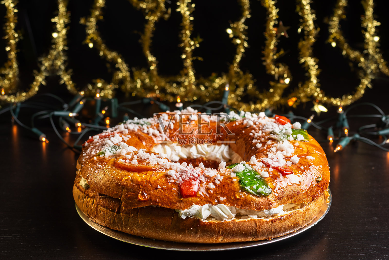 国王蛋糕，一种用面团制作的甜蜜罗斯孔，装饰有糖果水果并填充奶油，背景有圣诞装饰。照片摄影图片