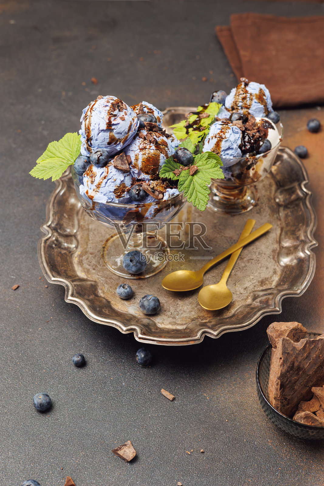 蓝莓冰淇淋盛在玻璃碗中，装饰有巧克力和配料，旁边有蓝莓果酱。背景为深色。夏季甜点。照片摄影图片