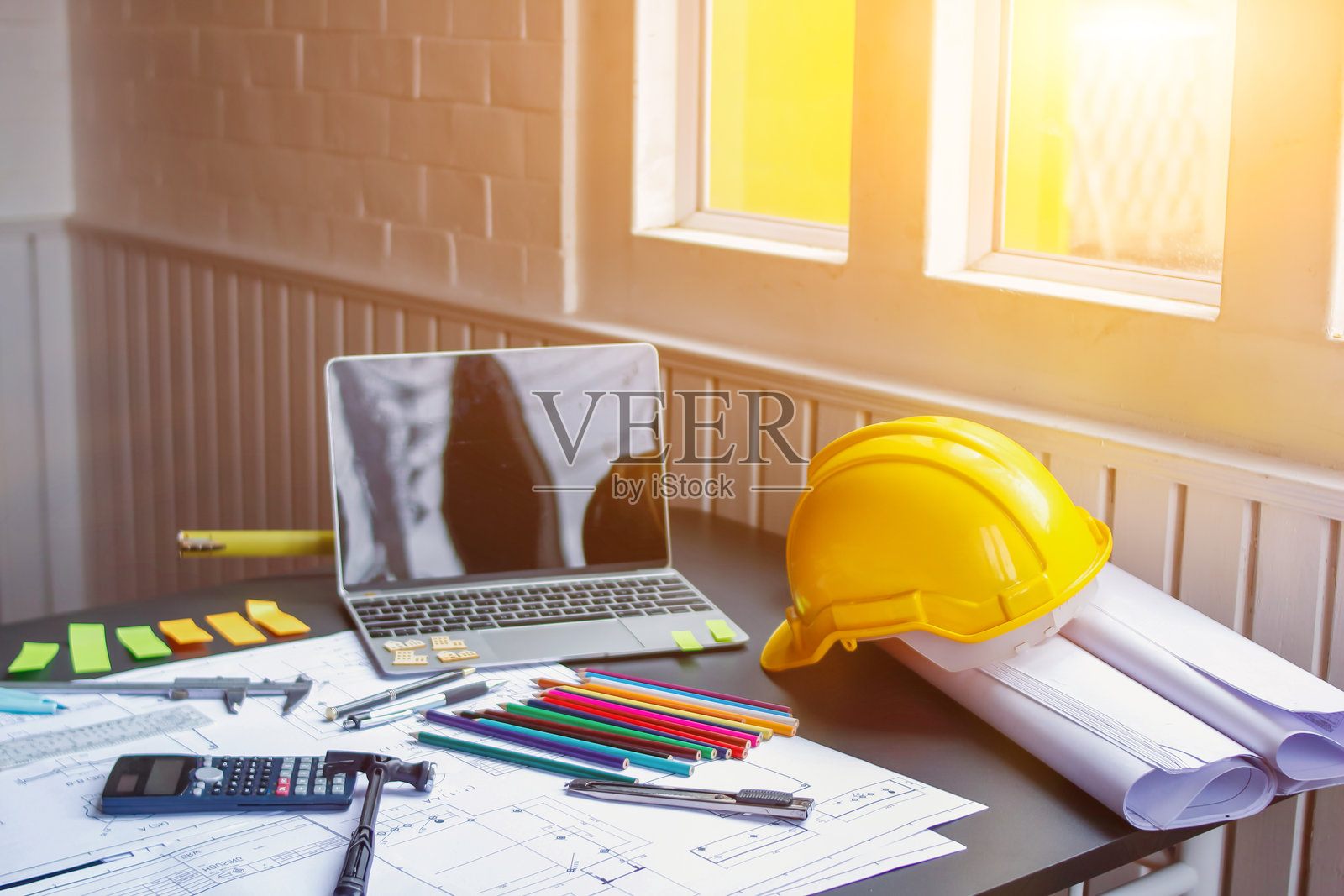 工程师和建筑师的桌子上摆满了蓝图、文具和电脑，桌上还有设备、文具、大量文件和一个安全帽。照片摄影图片