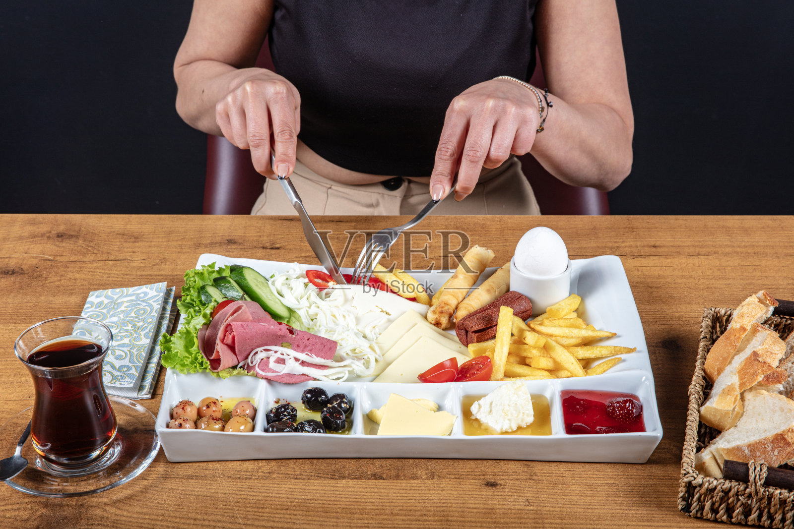 在餐厅做早餐的女士，土耳其早餐盘包括鸡蛋、面包、橄榄和沙拉。这位不易辨认的女士用刀叉享用她美味的餐点。照片摄影图片