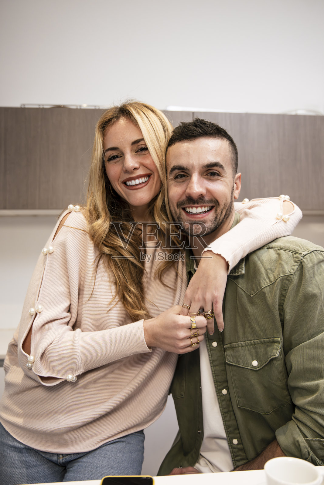 温馨微笑的年轻情侣在家中相拥，面向镜头。无忧无虑的男女在客厅中一起放松。照片摄影图片