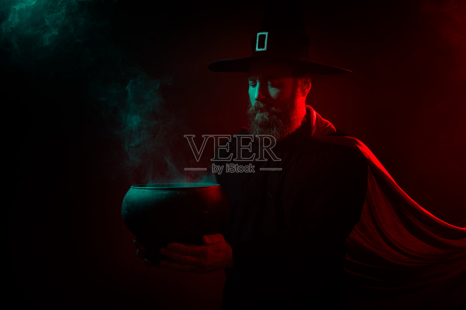 巫师在黑暗神秘的背景下，孤立地举着魔法锅进行万圣节的诡异仪式。照片摄影图片