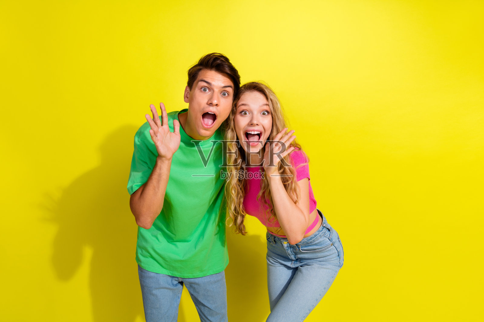 两位年轻人穿着T恤，面带惊讶，站在明亮的黄色背景前，身后是空旷的空间。照片摄影图片
