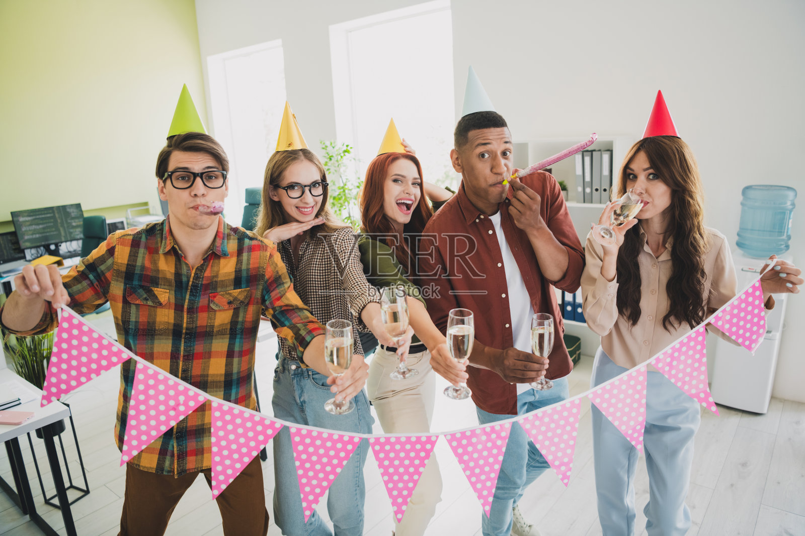 快乐的团队同事在办公室庆祝，手持粉色旗帜，戴着节日帽子，喝着葡萄酒。照片摄影图片