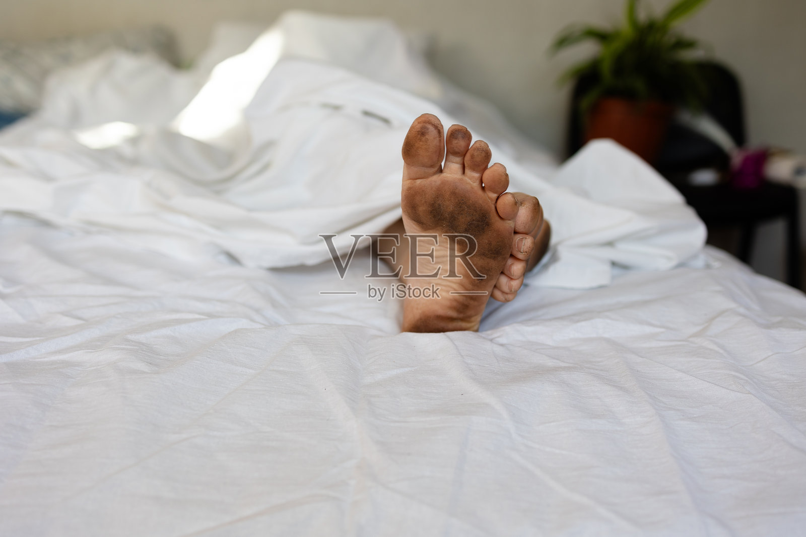 一个男人在雪白的床上睡觉，脚却非常脏。照片摄影图片