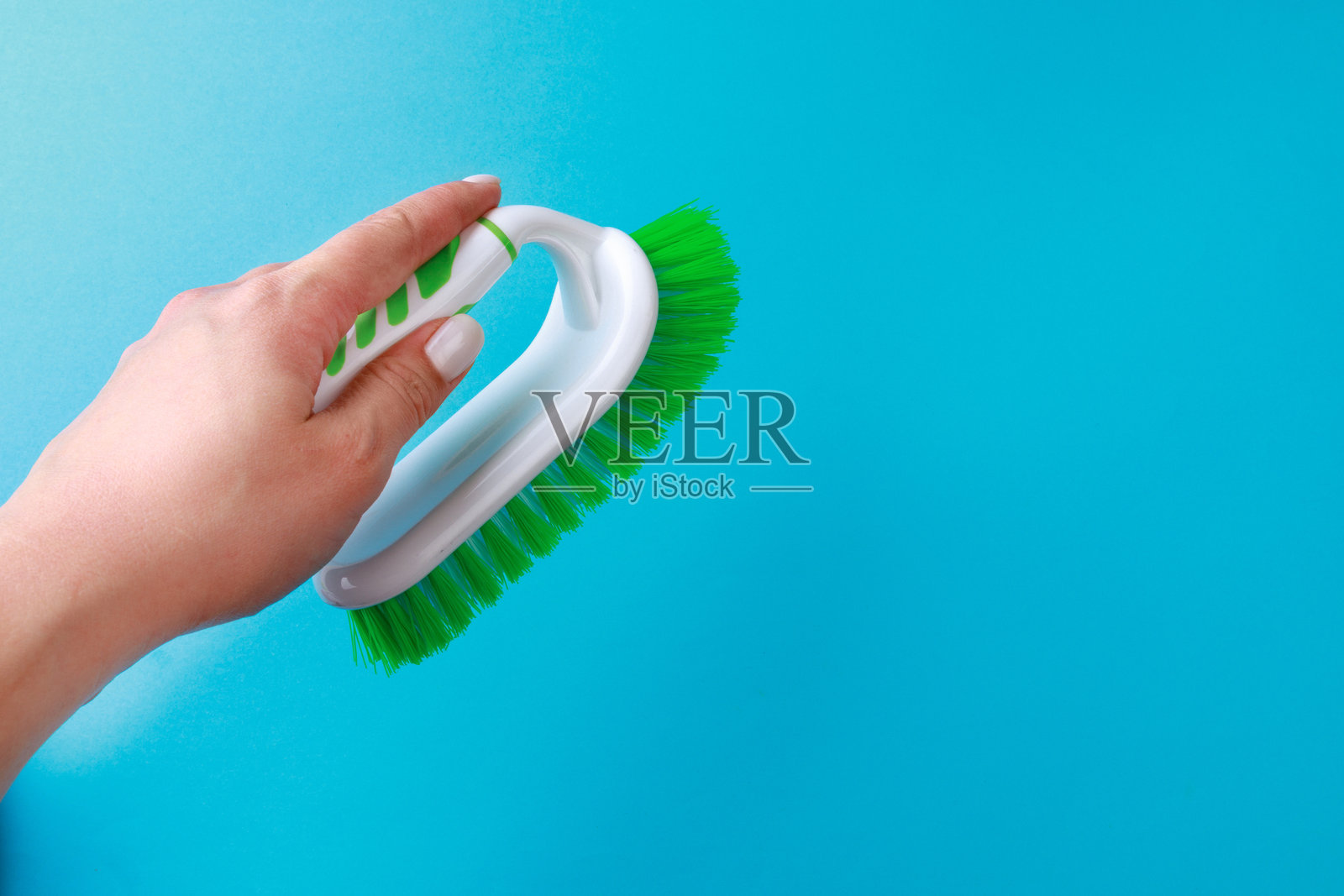 女人的手握着清洁刷，背景为彩色。用于清洁衣物和地毯的刷子。家居护理工具。照片摄影图片