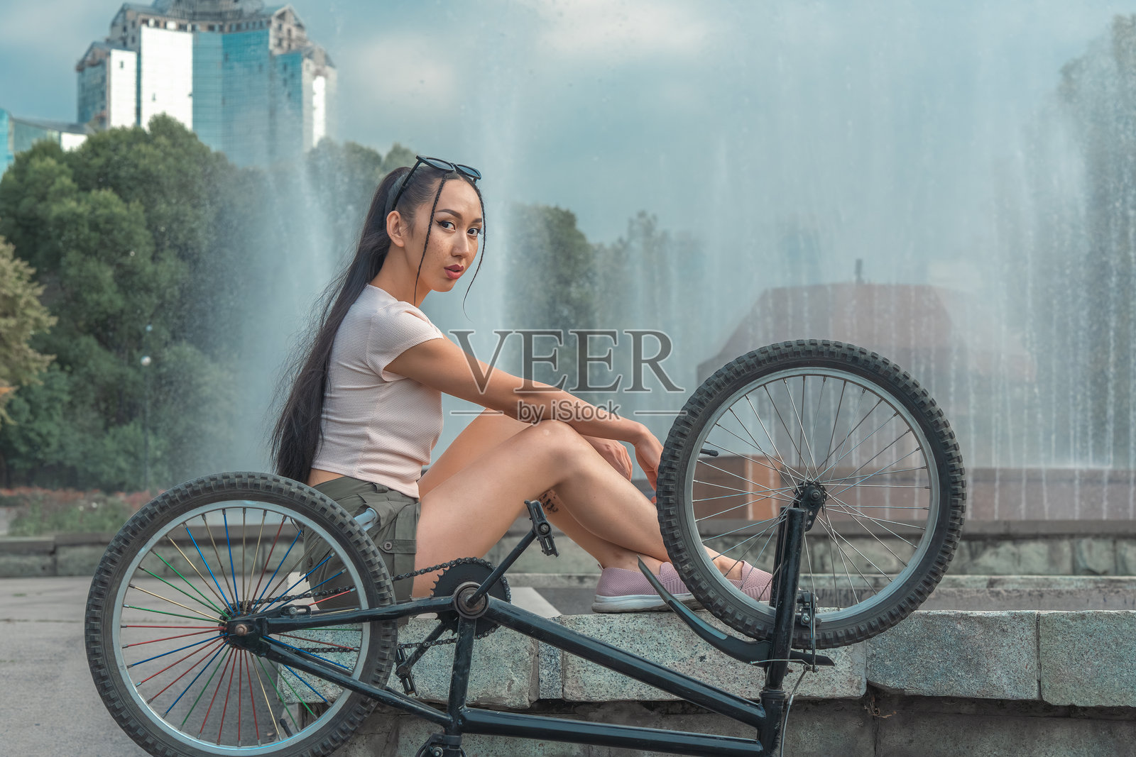 亚洲女孩骑着自行车坐在城市喷泉前。照片摄影图片