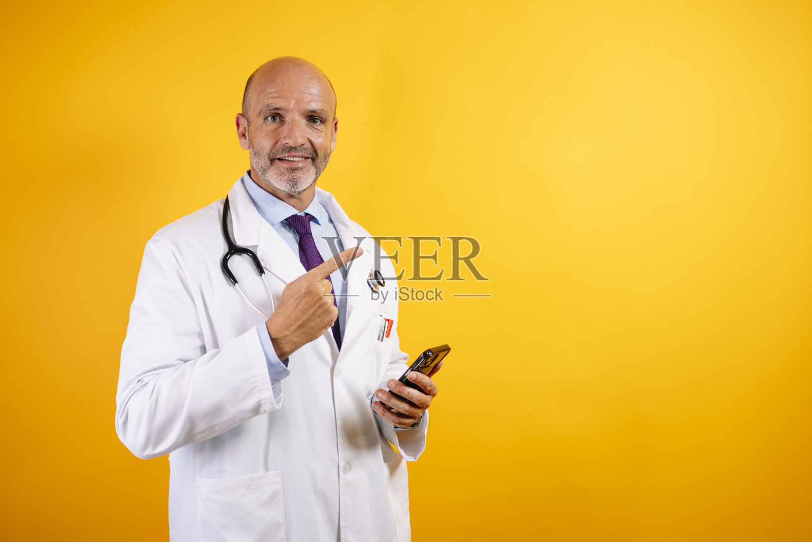 一位穿着白大褂的友好医生正在拿着智能手机，暗示现代医疗和沟通。照片摄影图片