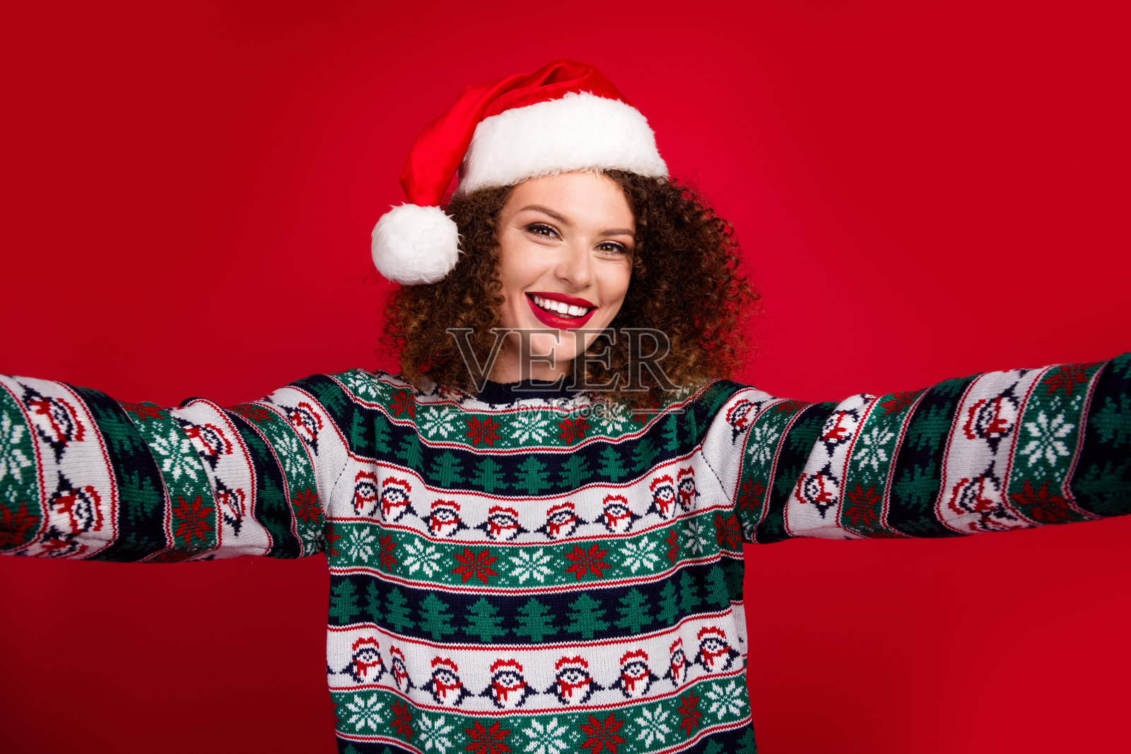 年轻女孩穿着新年圣诞毛衣自拍，背景为红色。照片摄影图片