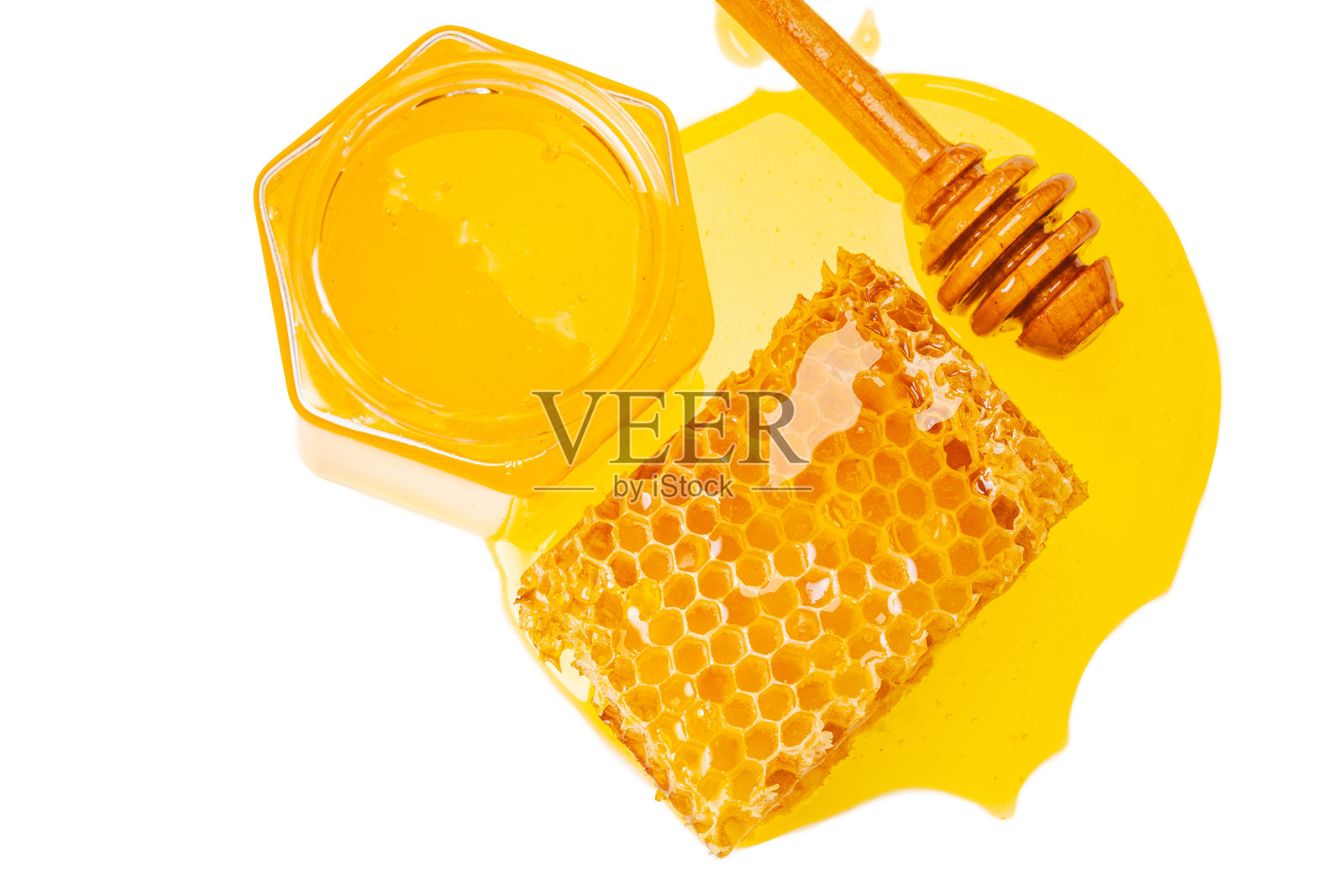 一个六角形玻璃罐，装有黄色甜蜜的蜂蜜、蜂巢和木制蜂蜜搅拌器，白色背景上有漏出的蜂蜜和留白空间。照片摄影图片