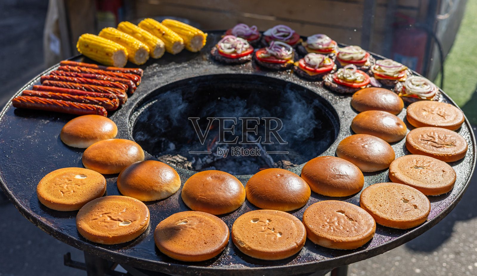 制作美味的汉堡。面包胚烤得恰到好处。汉堡肉饼在户外烤制，发出滋滋的声音。汉堡上搭配新鲜的配料。照片摄影图片