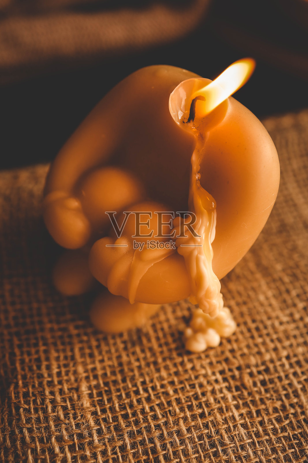 艺术形状的燃烧蜡烛，融化的蜡滴落下来，营造出温暖舒适的氛围，背景是质朴的布料。照片摄影图片