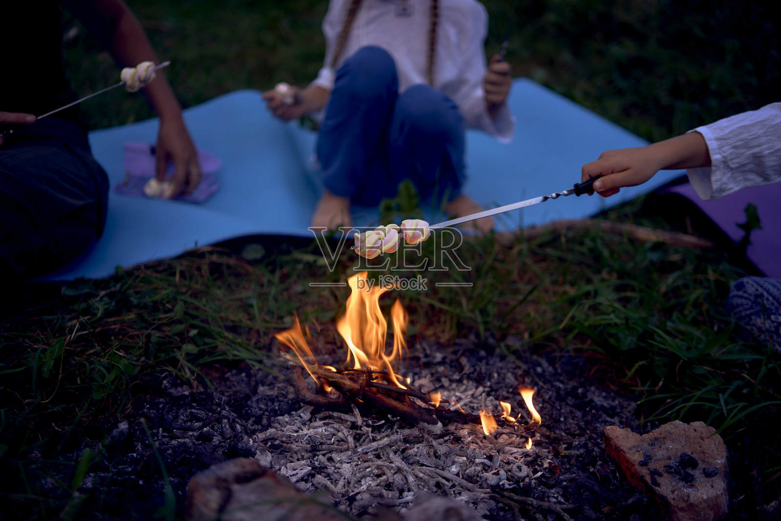 母亲和她的女儿们在篝火上烤棉花糖，享受与孩子们的露营假期。照片摄影图片