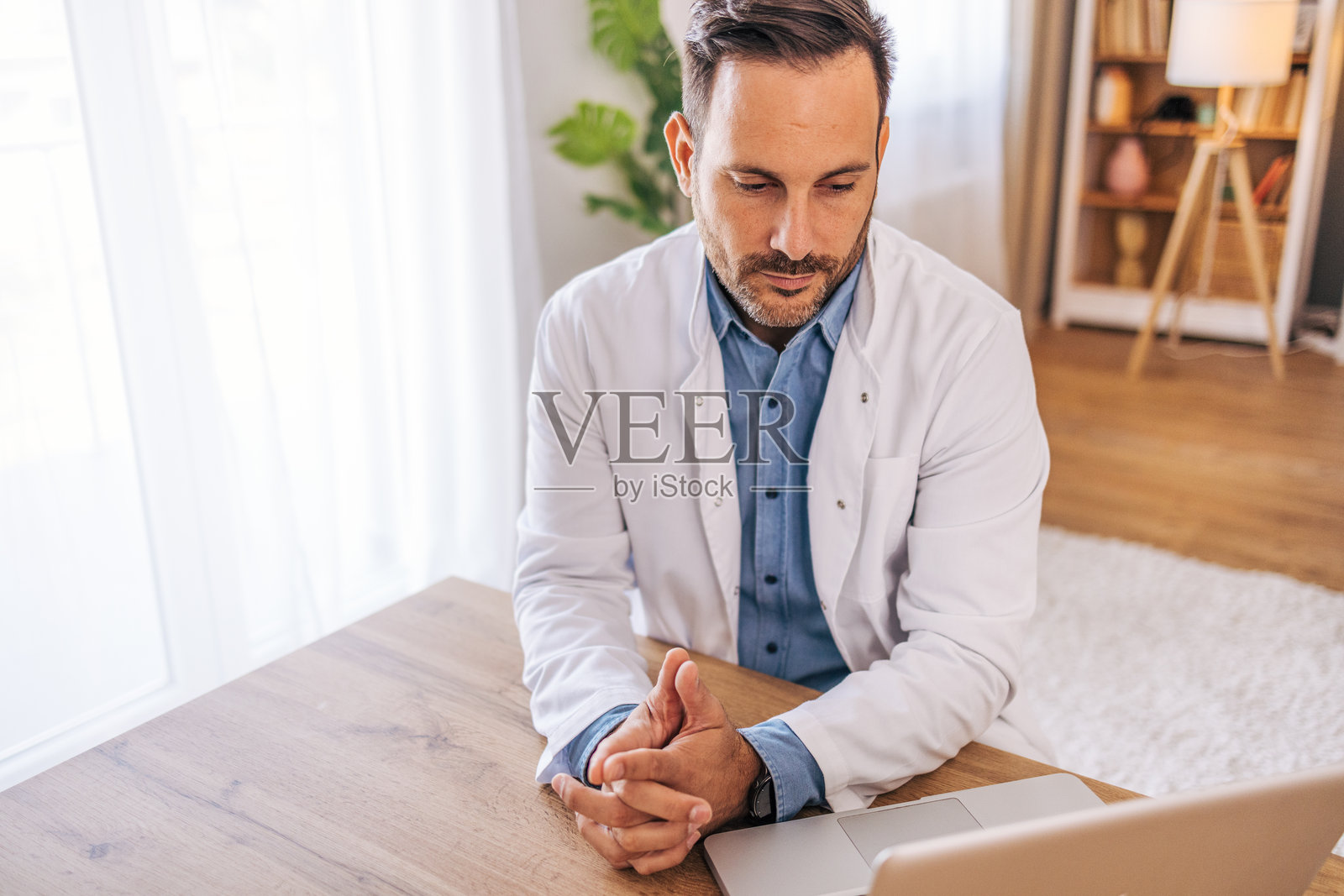 一位中年、开朗的男医生在家中的客厅使用笔记本电脑。照片摄影图片