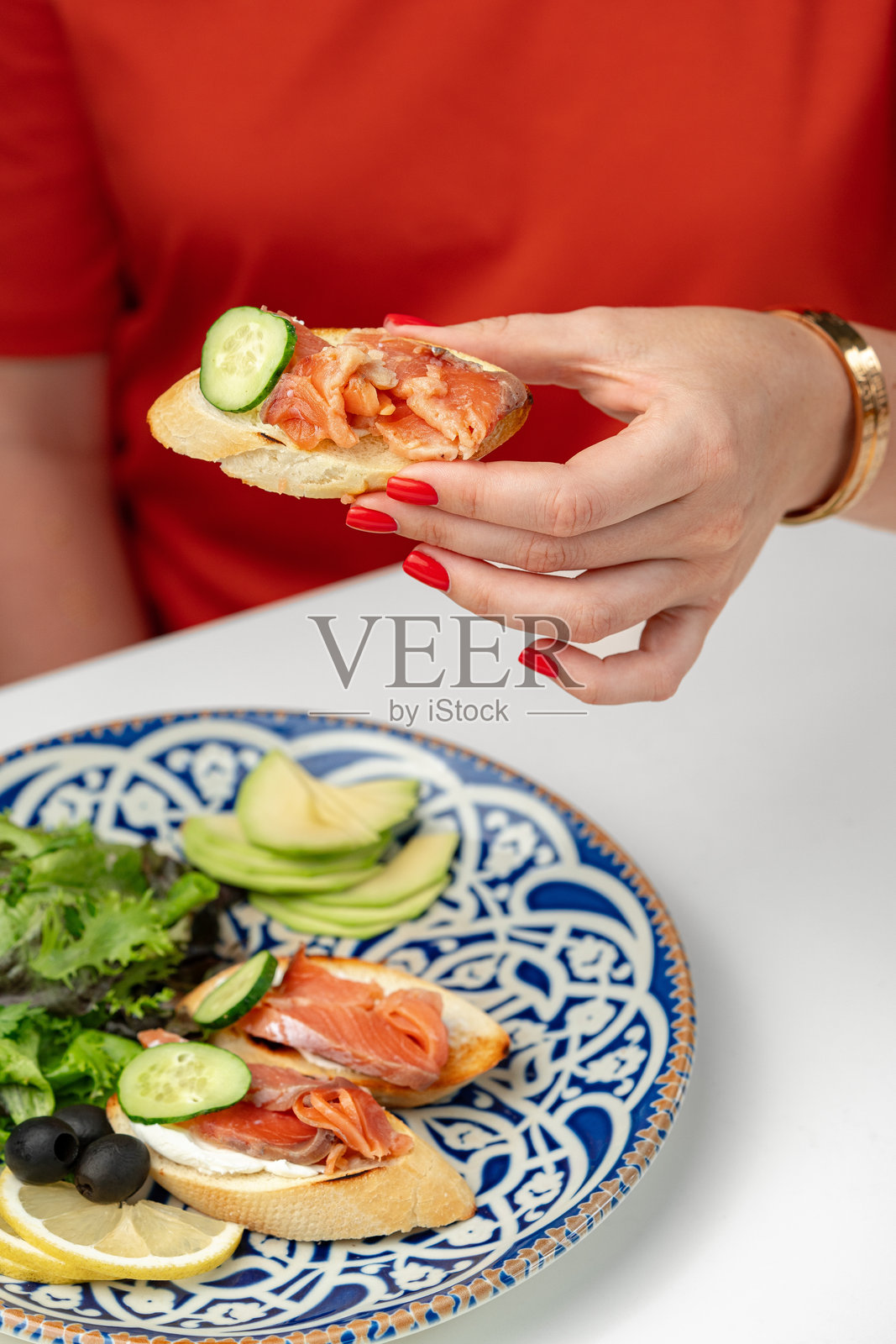 女人享用烟熏三文鱼和黄瓜的吐司小吃，搭配新鲜沙拉照片摄影图片