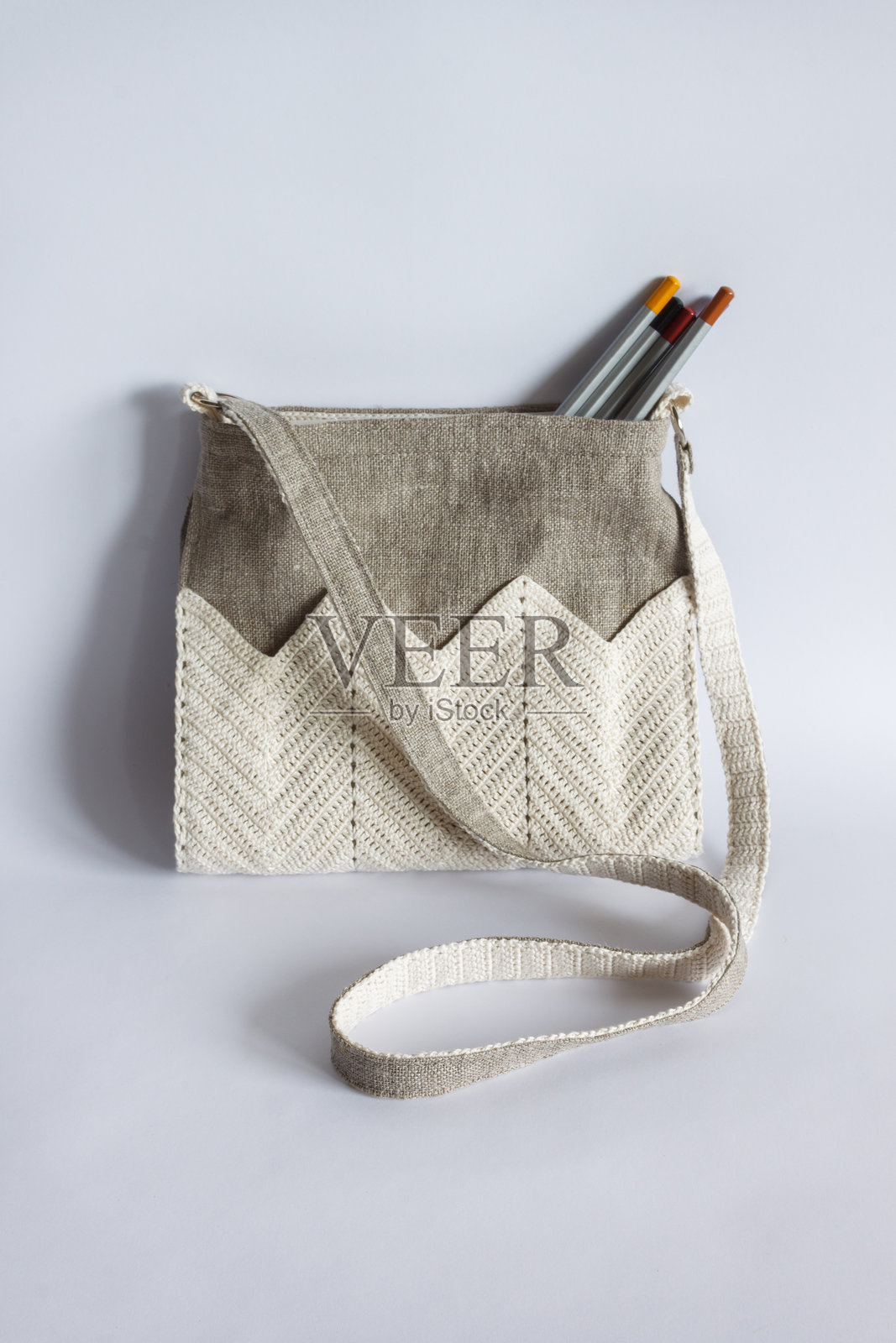 这款斜挎包由亚麻制成，装饰有编织的白色装饰。照片摄影图片