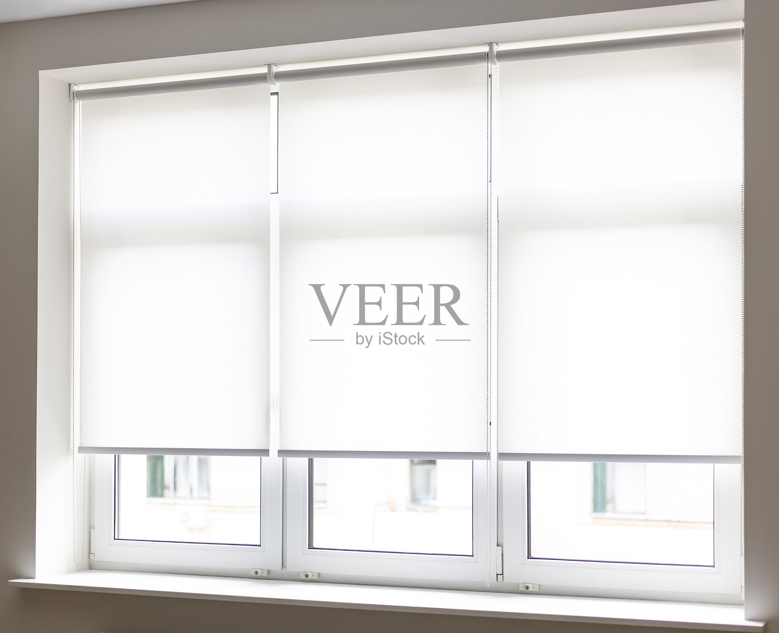 现代白色卷帘在明亮的房间里遮挡窗户，白天时分。照片摄影图片