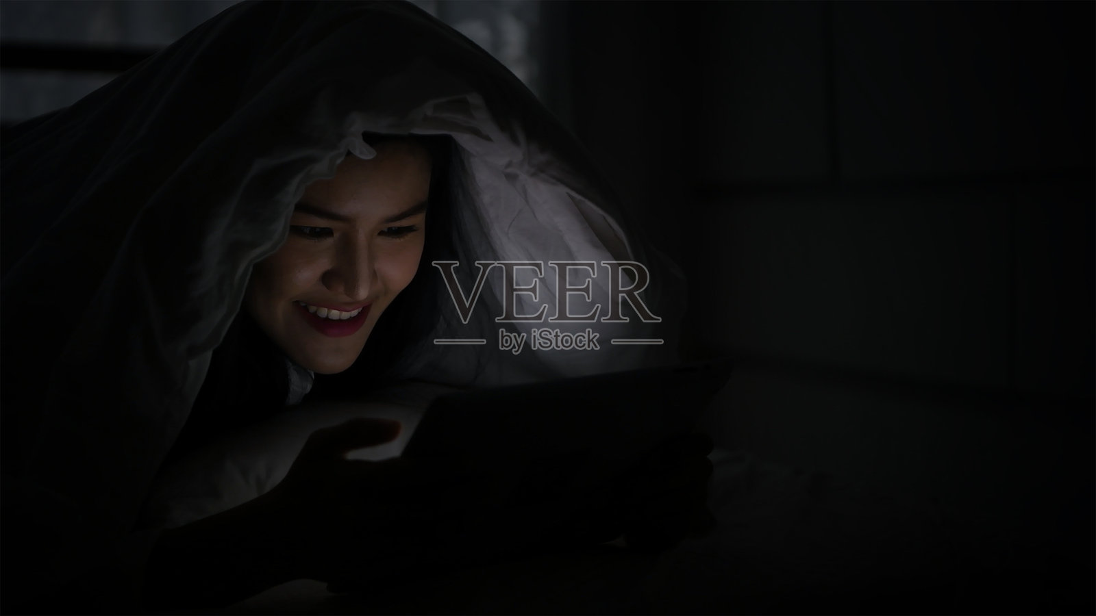 微笑的年轻女性在床上使用平板电脑照片摄影图片