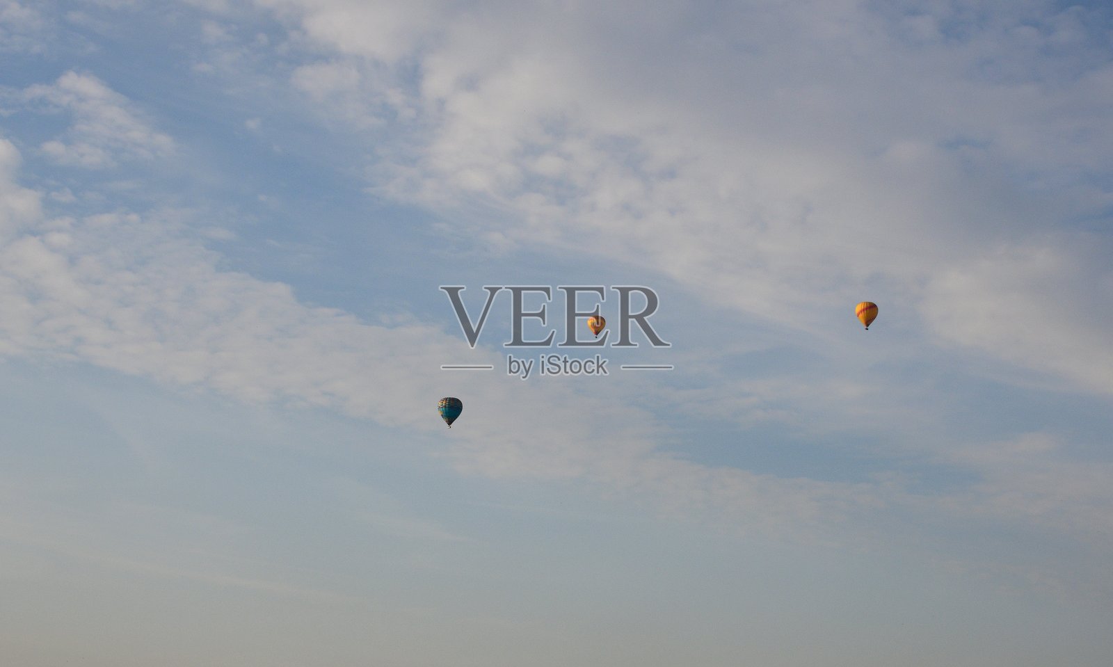 特写三只五彩缤纷的气球在多云的天空中飞翔，旁边有一些蓬松的云朵，远处是夏季波兰乡村日出时的小村庄。照片摄影图片