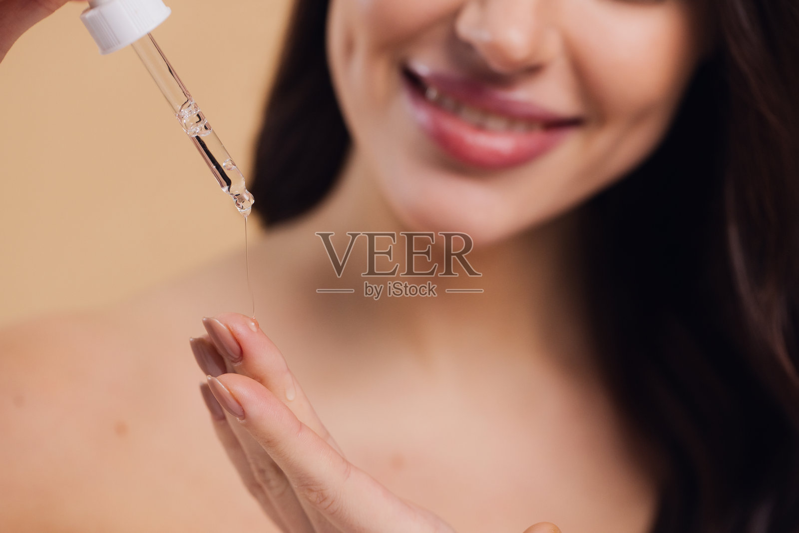 女性在米色背景下将精华液滴在脸上照片摄影图片