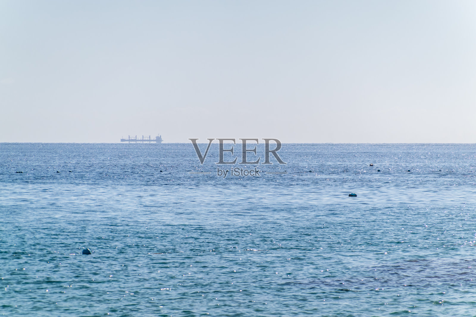 平静的蓝色海洋，远处地平线上有一艘大型船的轮廓照片摄影图片