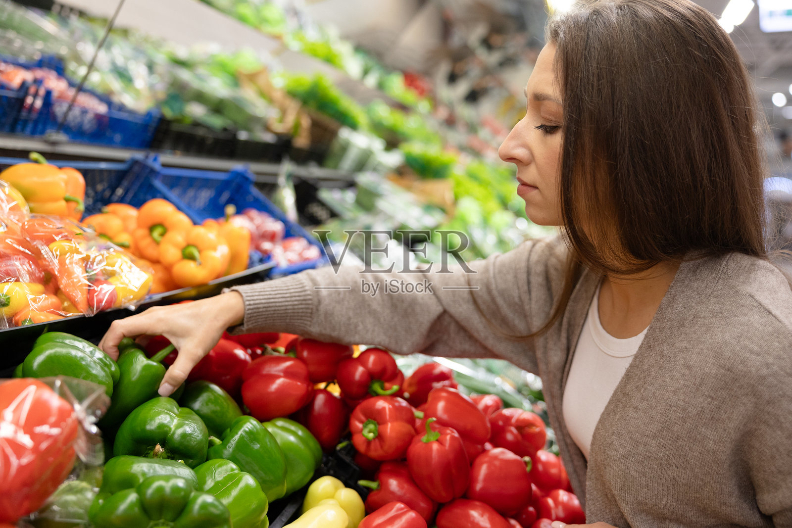 女性在超市蔬菜区挑选新鲜的绿色甜椒。健康饮食、购买天然产品和关注食品质量的理念。照片摄影图片