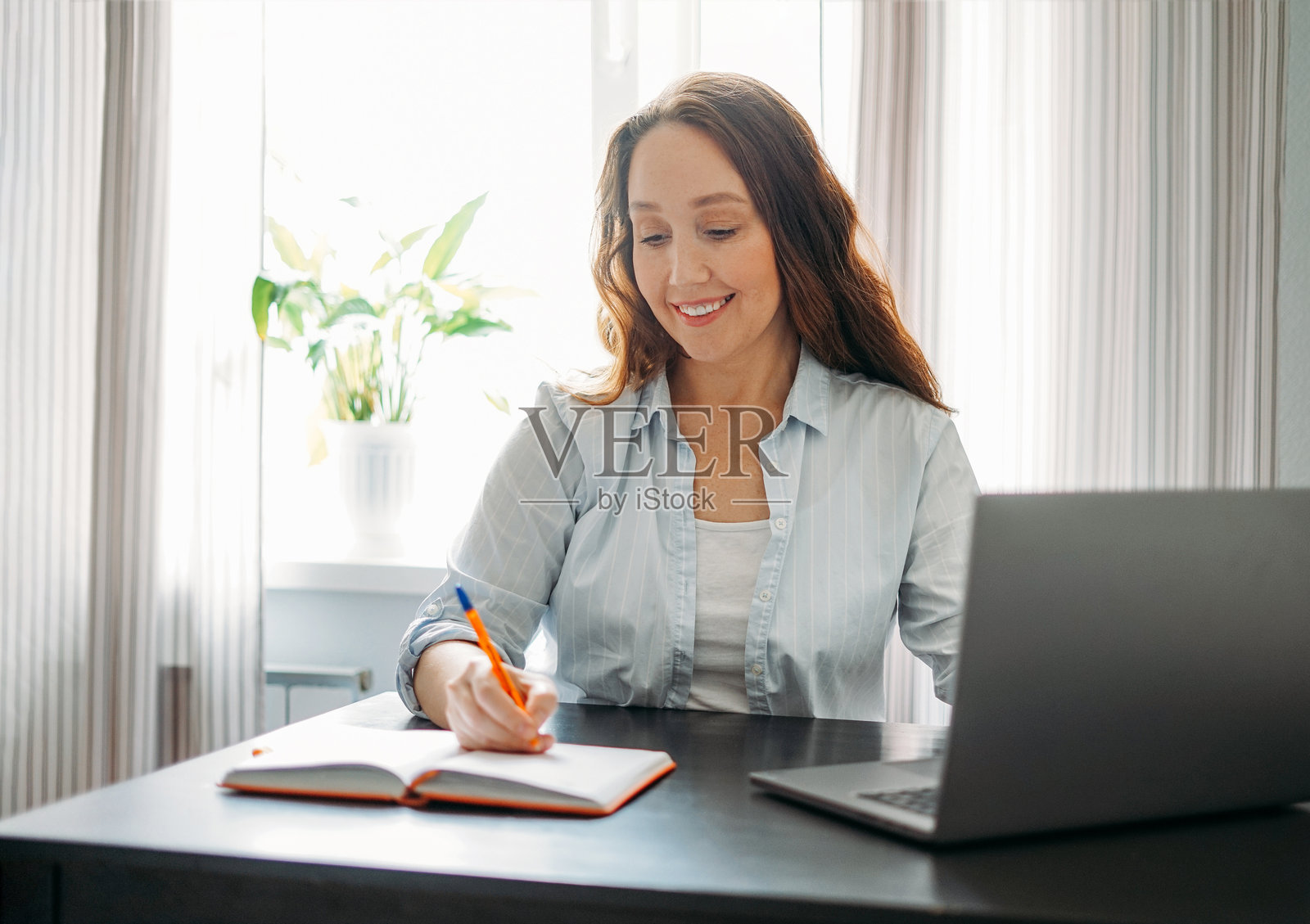 一位棕发成年女性在桌子上用打开的笔记本电脑做笔记照片摄影图片