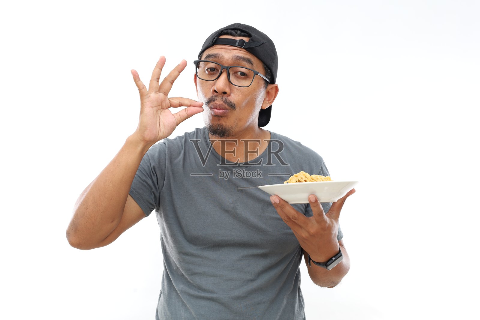 亚洲男子站着，手持一盘炒面，做出美味的手势。照片摄影图片