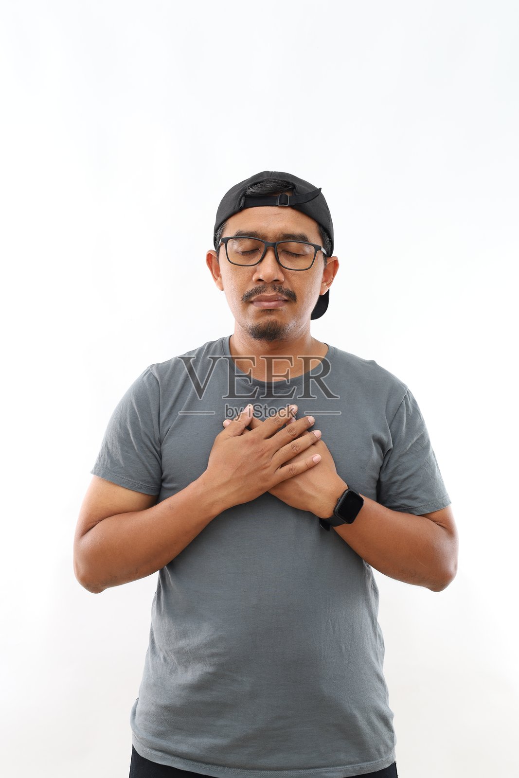 英俊的年轻亚洲男子在白色背景下，双手放在胸前，闭着眼睛，脸上带着感激的表情。健康概念。照片摄影图片