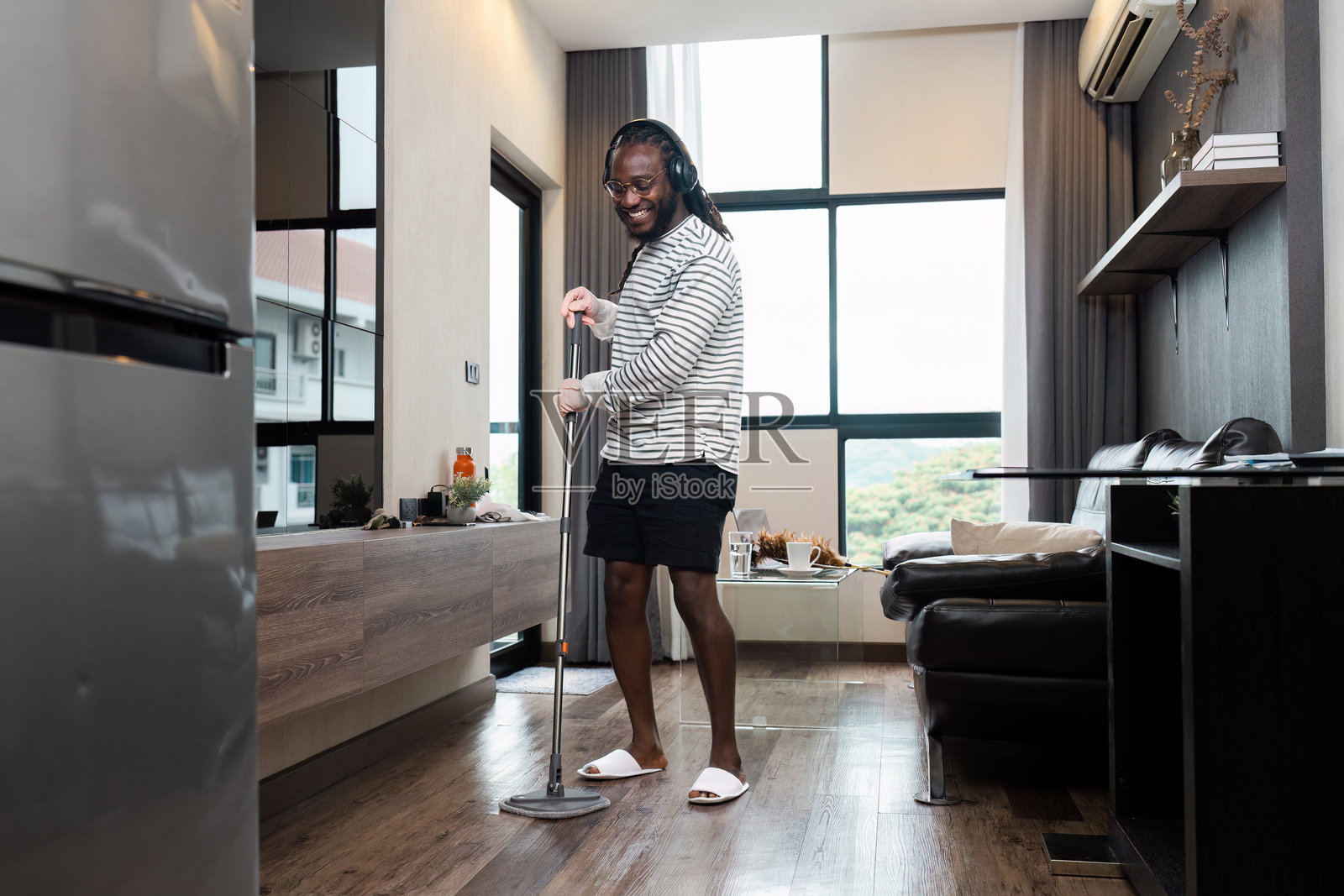 年轻男人在带大窗户和现代家具的客厅里拖地照片摄影图片