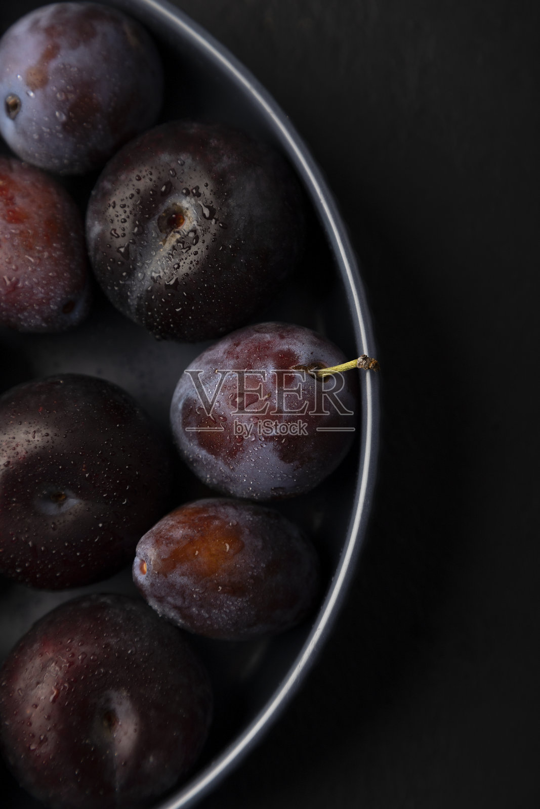 多汁成熟的新鲜李子，带有水滴，放在黑色背景的灰色盘子里。时令水果。选择性对焦，特写。照片摄影图片