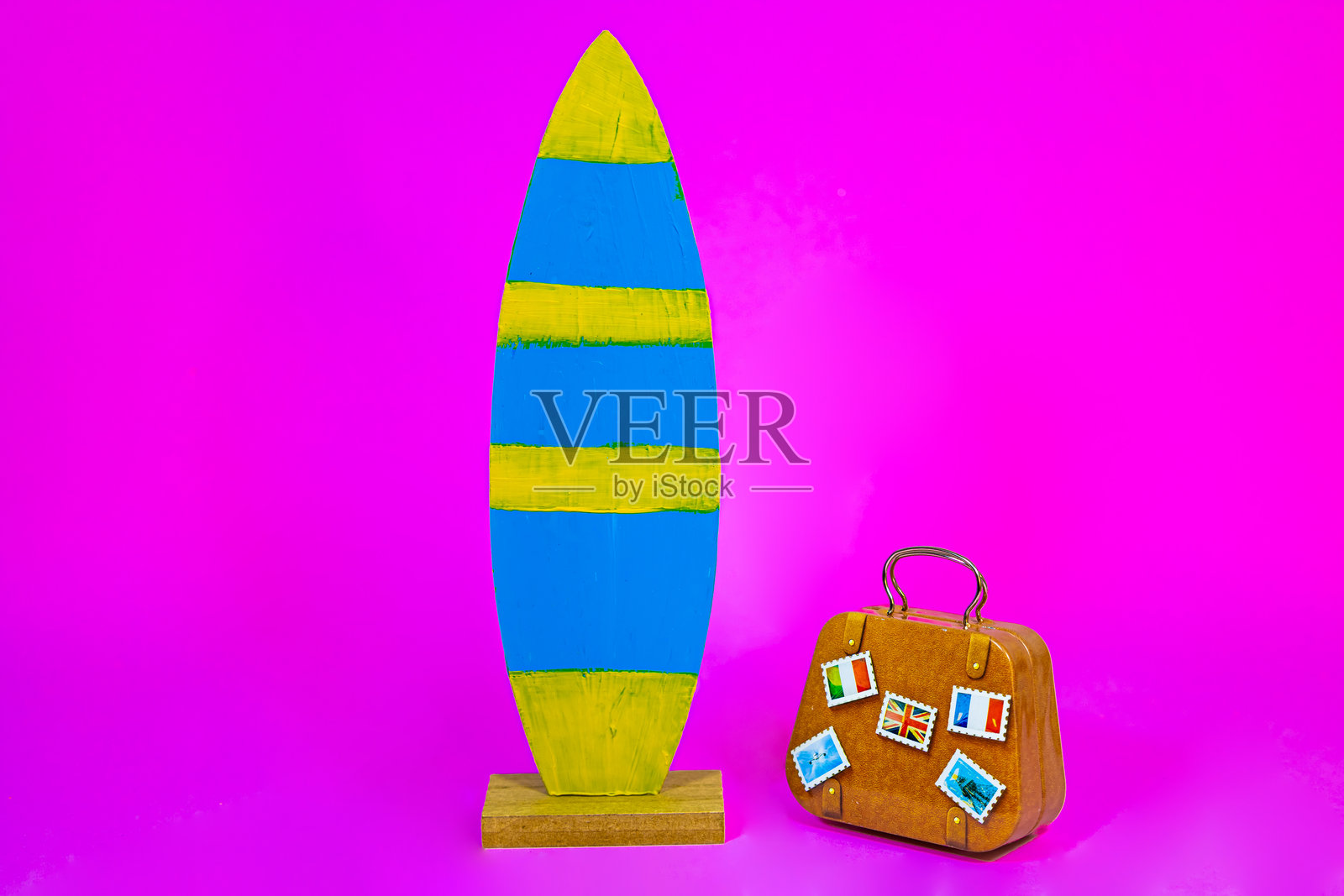 粉色背景上放着冲浪板和旅行箱照片摄影图片