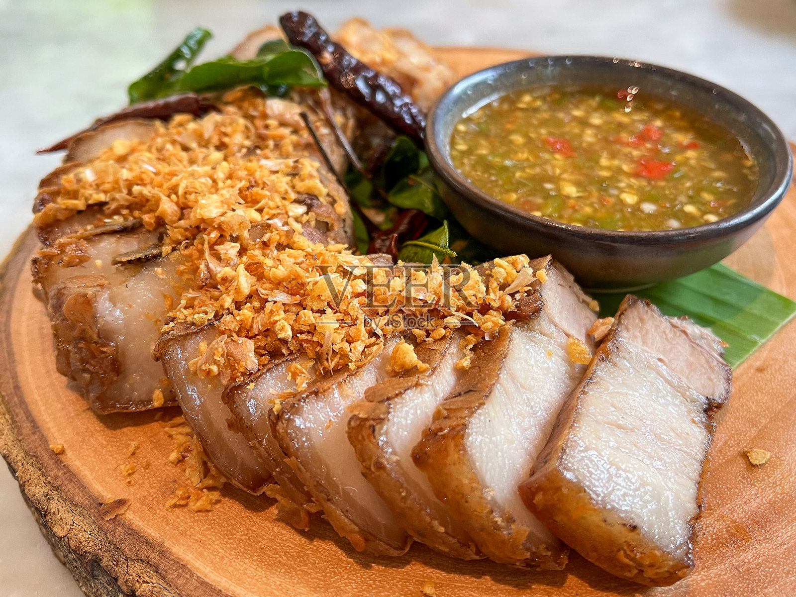 切片脆皮五花肉，配以辛辣的蘸酱和新鲜香草，摆放在木质托盘上。照片摄影图片