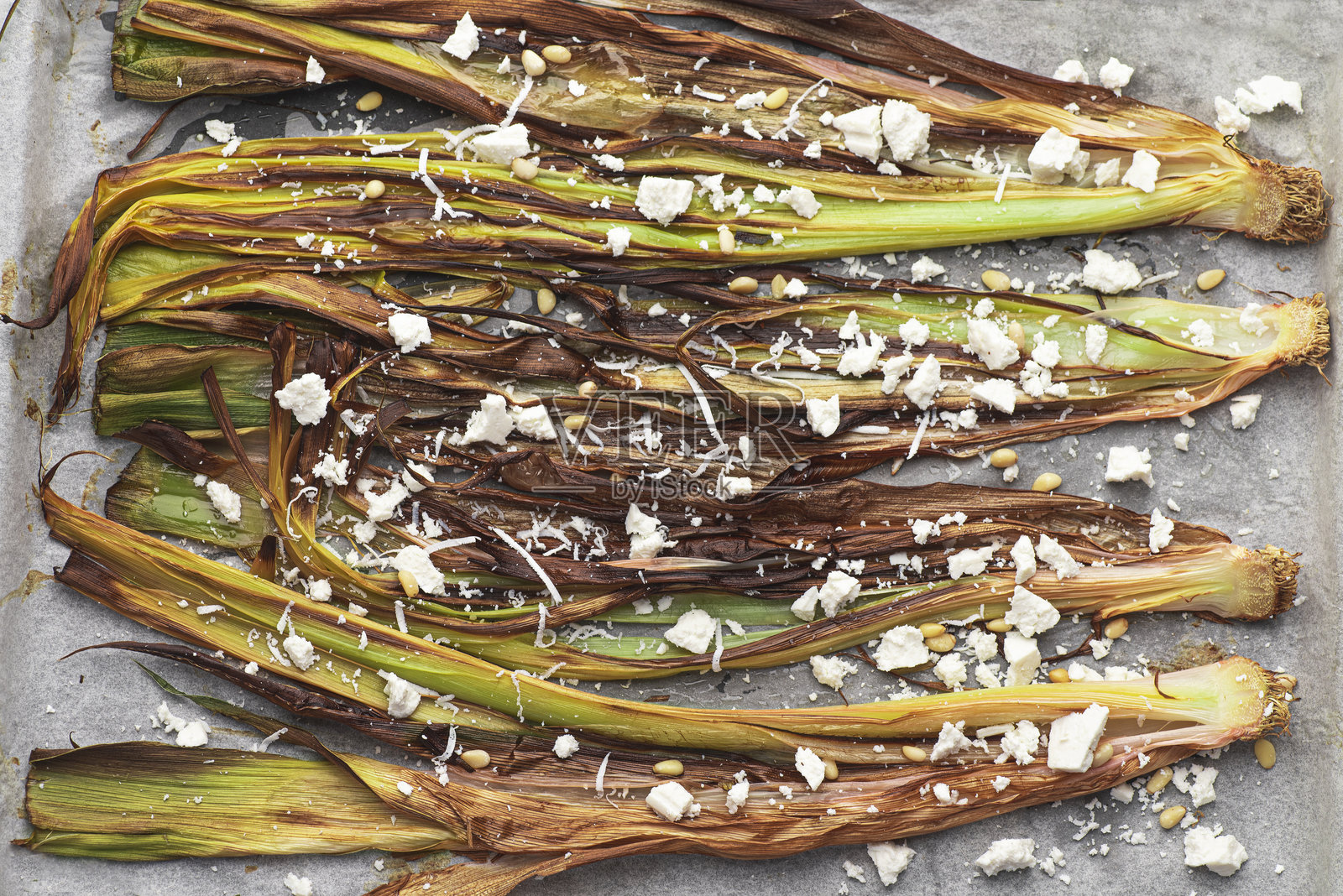 烤韭葱，撒上奶酪和松子。作为配菜或食谱的一部分，适合做馅饼、汤或混合蔬菜。健康的自制食品，食品背景。照片摄影图片