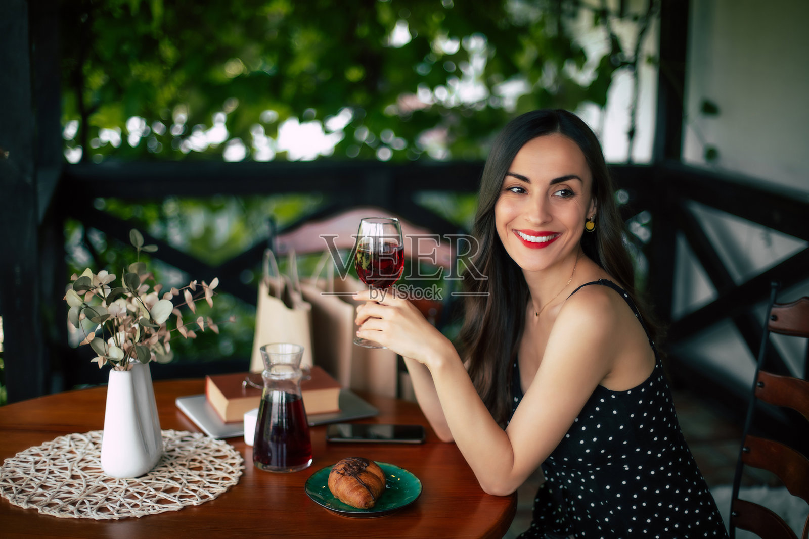 微笑，华丽，感性，沉思，浪漫，迷人的年轻黑发女子，时尚的发型和晚装，穿着黑色礼服，坐在咖啡馆里喝红酒照片摄影图片